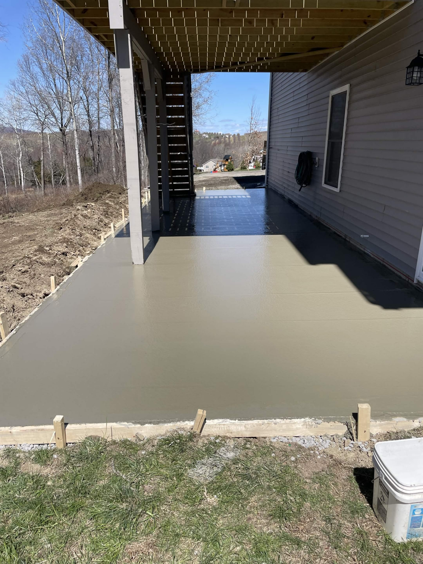 Freshly poured and finished concrete patio slab beneath a deck