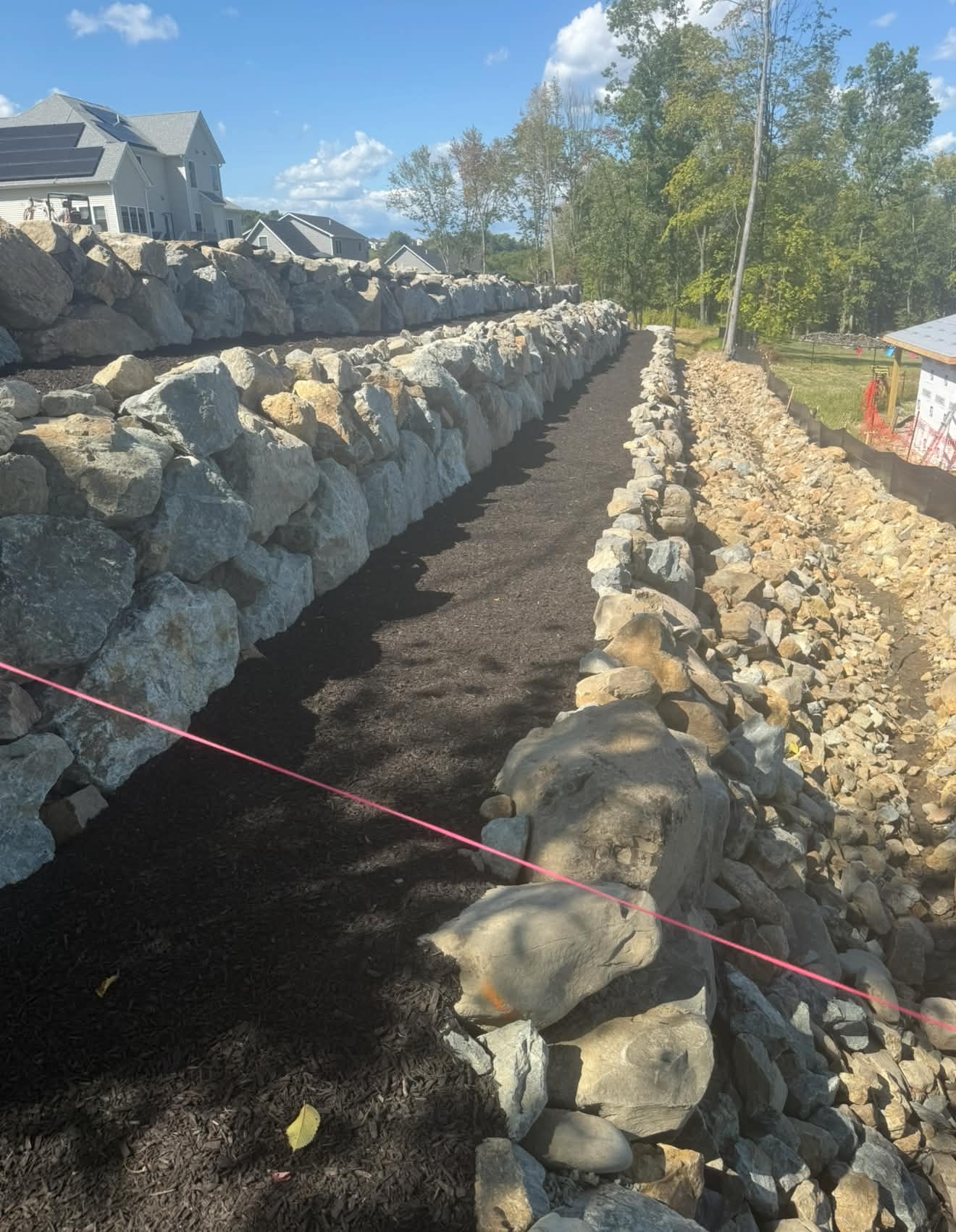 Boulder retaining wall built alongside a drainage trench
